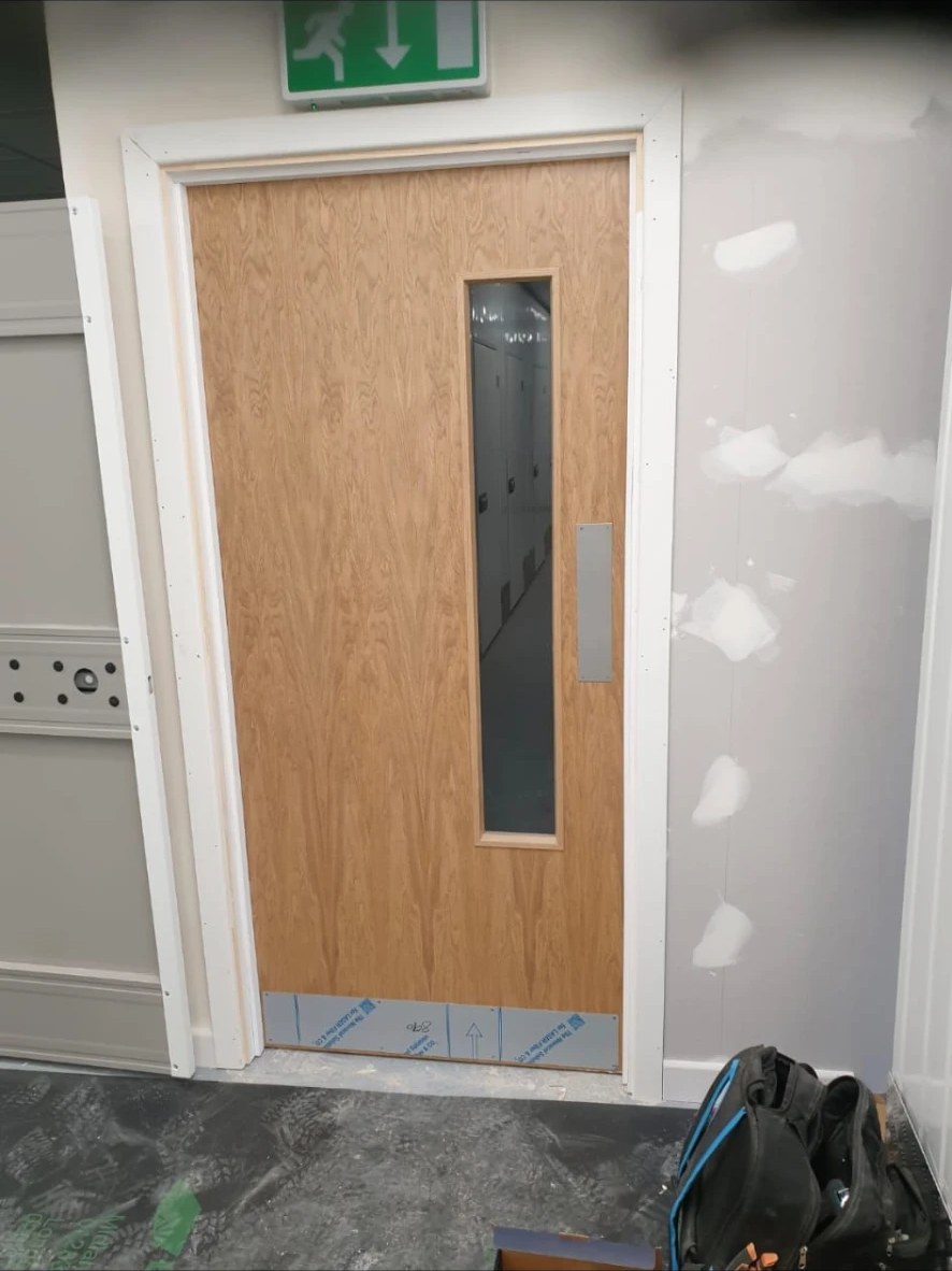 Oak vision-panel fire door installed in a painted frame on a commercial fit out